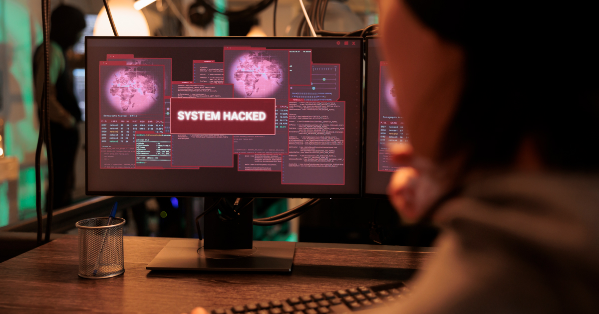 Person monitoring "System Hacked" alert on computer screen.